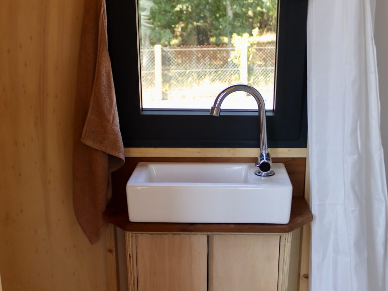 Meuble de salle d’eau en bois avec vasque et robinet noir sous la fenêtre
