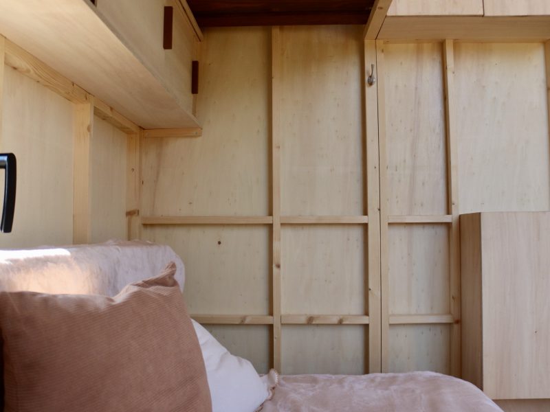 Rangements en bois intégrés près du lit dans le studio mobile TYMUP